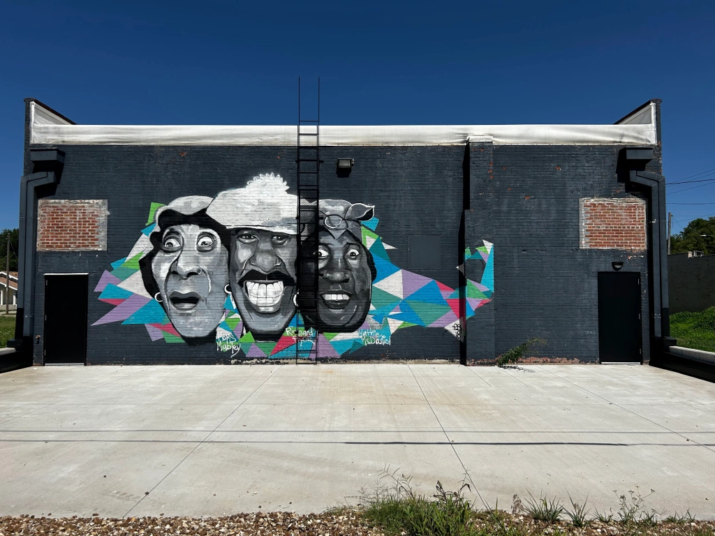 A mural featuring three black and white faces on a multi-colored background, painted on a black building.