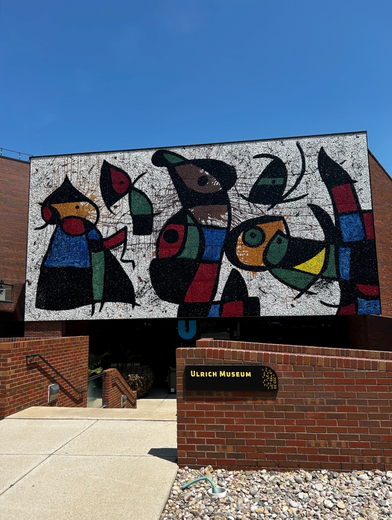 A mural showing abstract, multi-colored figures. A sign indicates that the building it is painted on is the Ulrich Museum.